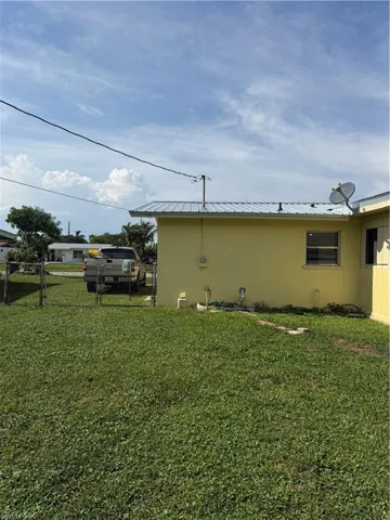 Grassed yard area featuring a chain-link fence, leading to a light yellow exterior wall with a window
