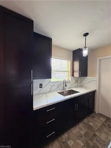 Kitchen featuring dark wood cabinetry, white stone countertops with integrated backsplash, stainless steel undermount sink, and a modern pendant light fixture