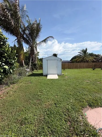 Expansive backyard featuring a white storage shed with a concrete pad, a chain-link fence, and mature palm trees