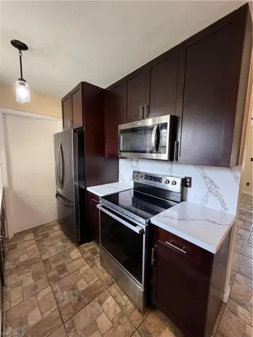 Contemporary kitchen featuring rich wood-finish cabinetry, stainless steel appliances, white quartz countertops, and a decorative tile backsplash