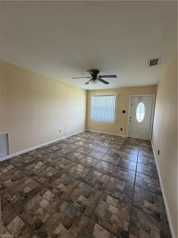 Spacious room featuring mosaic-patterned tile flooring, a window with horizontal blinds, and a white entry door with an oval-shaped glass insert