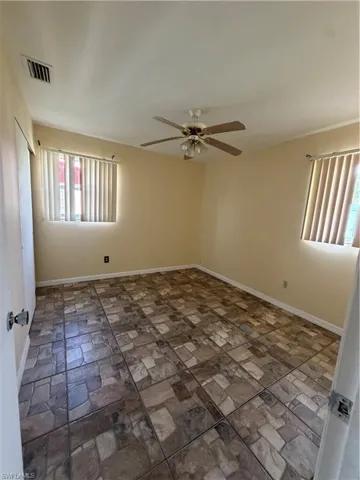 Spacious room featuring patterned tile flooring, a ceiling fan with integrated lighting, and two windows with vertical blinds
