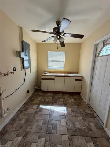Utility room featuring a patterned tile floor, built-in cabinetry with a countertop, a ceiling fan with light fixture, and a window with blinds