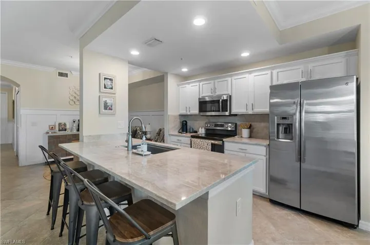 Kitchen with white cabinetry, kitchen peninsula, stainless steel appliances, decorative backsplash, and sink