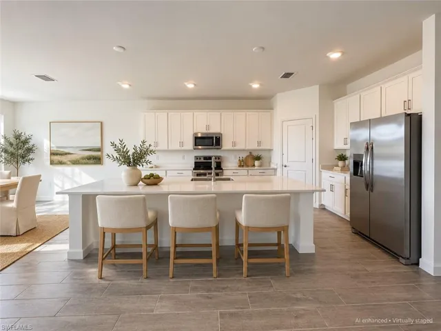 Kitchen featuring a large island with counter seating, white cabinetry, integrated stainless steel appliances, and tile flooring