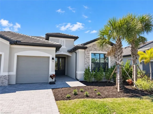Exterior featuring a tiled roof, stone facade accents, paver driveway, and mature landscaping