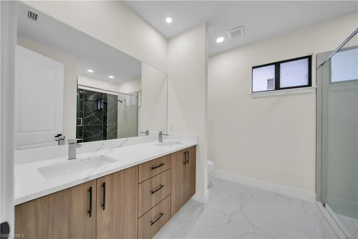 Bathroom featuring a marble finish shower, double vanity, light marble finish flooring, and recessed lighting