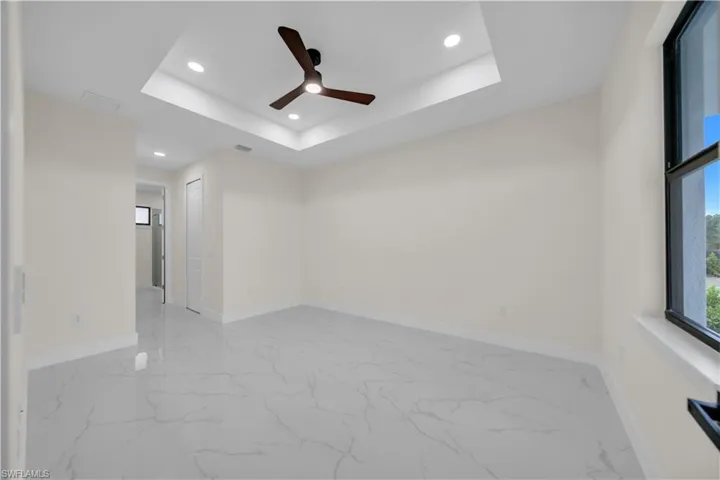 Unfurnished room featuring recessed lighting, light marble finish floors, a ceiling fan, and a raised ceiling