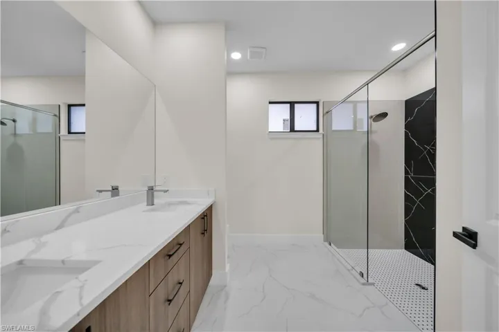 Bathroom featuring a marble finish shower, double vanity, light marble finish floors, and recessed lighting