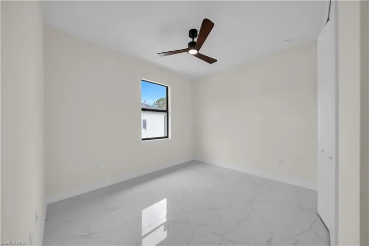 Empty room featuring marble look tiles and a ceiling fan