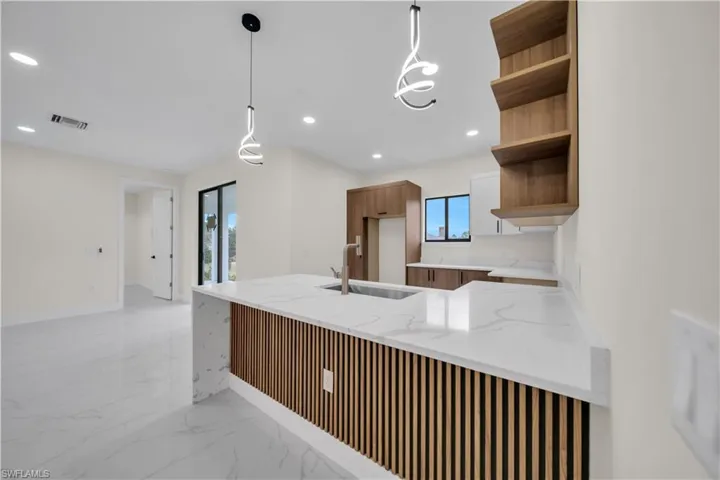 Kitchen with light stone countertops, a peninsula, hanging light fixtures, open shelves, and light marble finish flooring