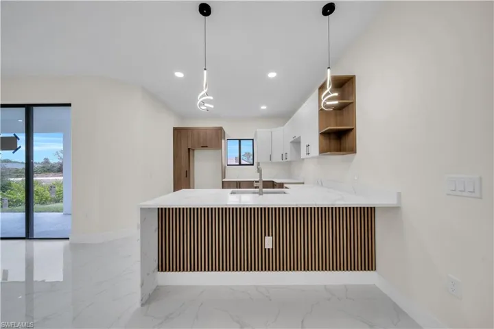 Kitchen with light stone countertops, hanging light fixtures, a peninsula, light marble finish floors, and open shelves