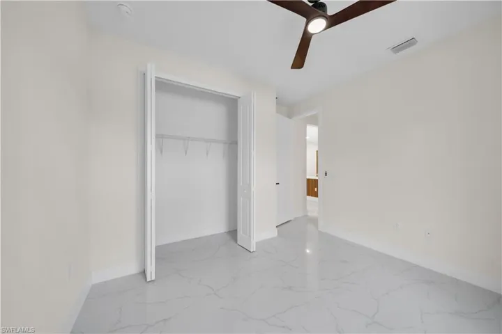 Unfurnished bedroom with a ceiling fan, light marble finish flooring, and a closet