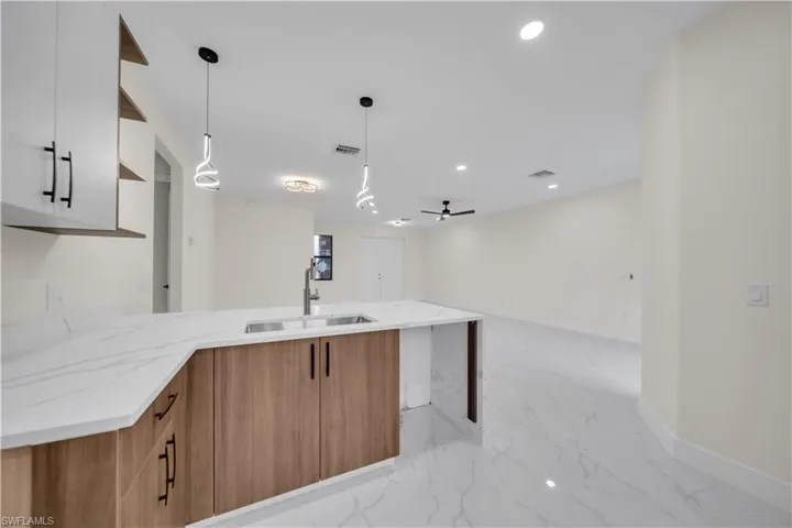 Kitchen with light stone countertops, wood finish cabinets, open floor plan, decorative light fixtures, and a peninsula