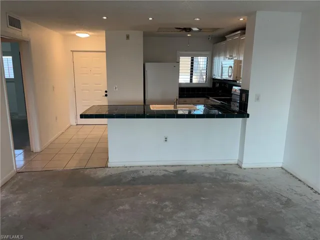 Kitchen with tile countertops, sink, white cabinets, kitchen peninsula, and stainless steel appliances