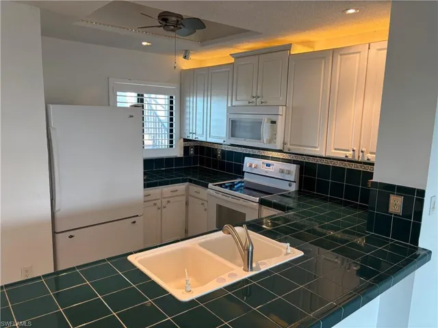 Kitchen featuring white cabinetry, sink, backsplash, tile counters, and white appliances