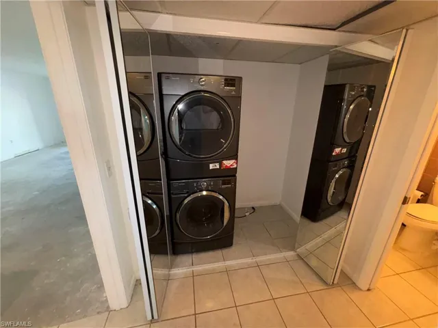 Laundry area with stacked washing maching and dryer and light tile patterned floors