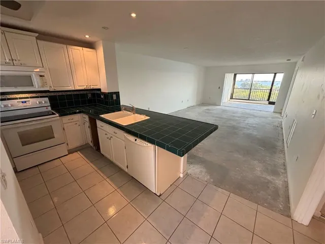 Kitchen featuring sink, white cabinetry, tile counters, kitchen peninsula, and white appliances