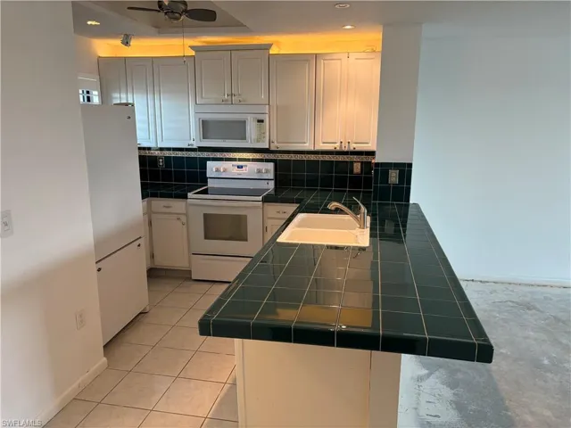 Kitchen featuring sink, white appliances, decorative backsplash, tile countertops, and kitchen peninsula