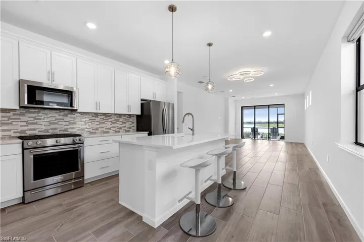 Kitchen featuring stainless steel appliances, wood finish floors, white cabinetry, and a kitchen island with sink