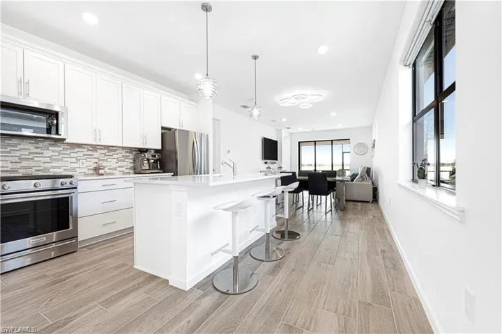 Kitchen with stainless steel appliances, a kitchen bar, open floor plan, white cabinets, and an island with sink