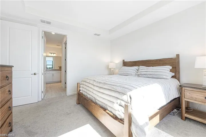 Bedroom with light colored carpet, a raised ceiling, and ensuite bathroom