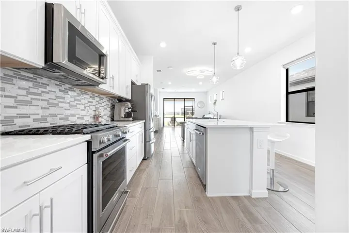 Kitchen with stainless steel appliances, white cabinets, light wood-style floors, pendant lighting, and a center island with sink