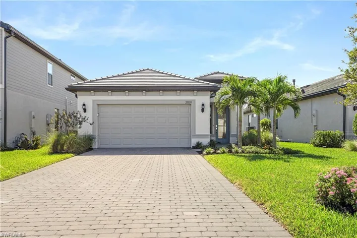 View of front of property featuring decorative driveway, an attached garage, a front lawn, and stucco siding