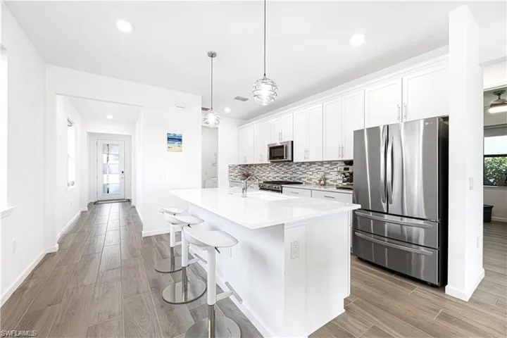 Kitchen with stainless steel appliances, white cabinetry, a kitchen bar, and wood finish floors
