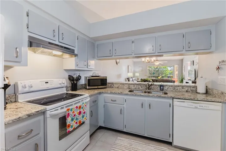 Kitchen featuring white appliances, gray cabinets, under cabinet range hood, light stone countertops, and light tile patterned floors
