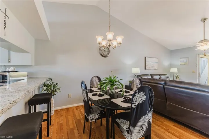 Dining space with vaulted ceiling, light wood finished floors, a chandelier, and ceiling fan