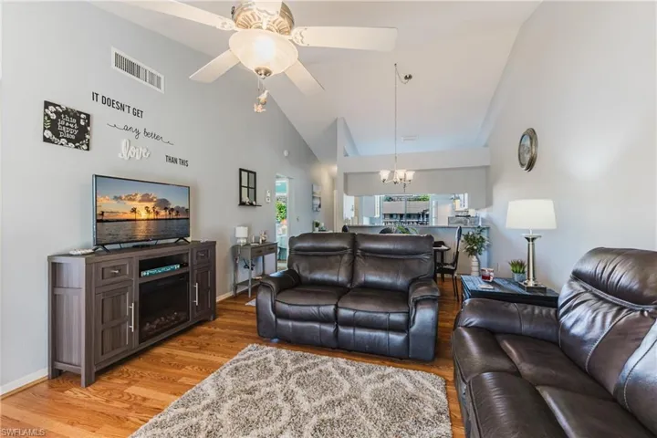 Living room featuring light wood finished floors, a chandelier, a ceiling fan, high vaulted ceiling, and a fireplace