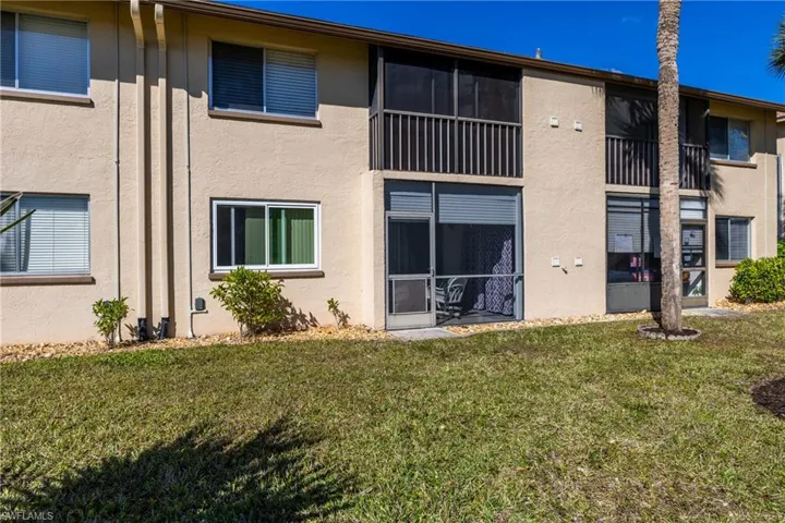 Rear view of property with stucco siding, a lawn, a balcony, and a sunroom