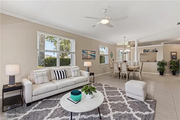 Virtually staged. Open-concept living and dining areas featuring tile flooring, neutral wall tones, multiple windows with blinds, a ceiling fan, and crown molding