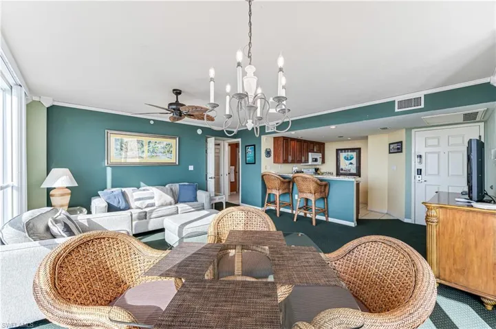 Carpeted living room featuring ornamental molding and ceiling fan with notable chandelier - VIRTUALLY ENHANCED