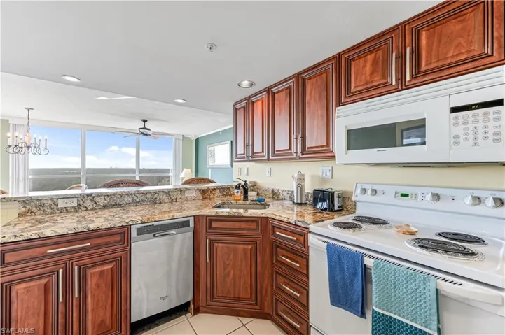 Kitchen featuring white appliances, sink, ceiling fan with notable chandelier, decorative light fixtures, and light tile patterned floors - VIRTUALLY ENHANCED
