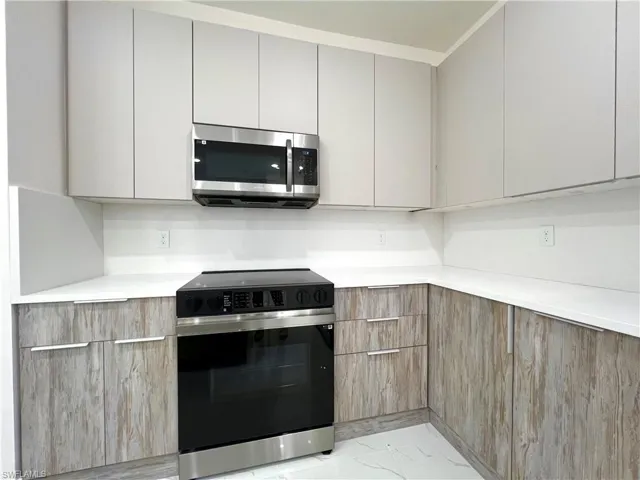 Kitchen with stainless steel appliances, gray cabinets, crown molding, and light tile floors