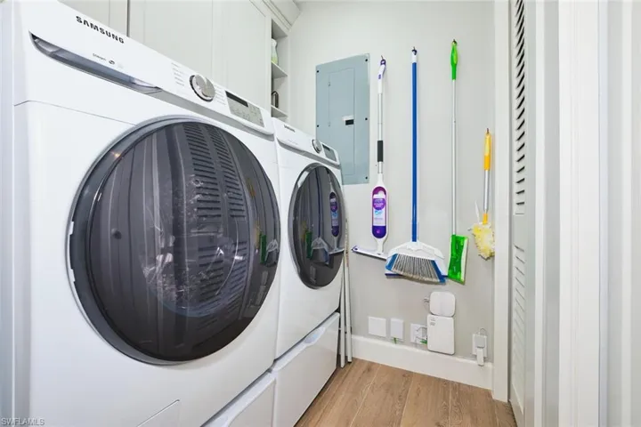 Laundry room featuring separate washer and dryer, light wood-type flooring, electric panel, and cabinet space