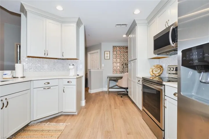 Kitchen featuring stainless steel appliances, white cabinets, decorative backsplash, an office area, and recessed lighting