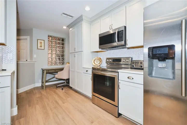 Kitchen with tasteful backsplash, appliances with stainless steel finishes, light countertops, white cabinetry, and light wood-type flooring