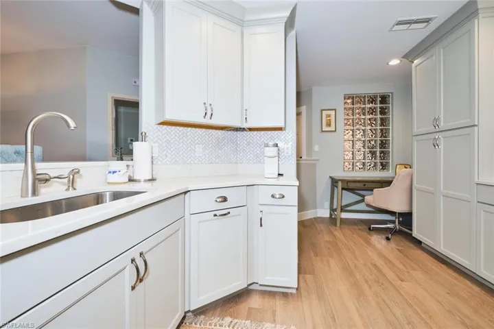 Kitchen with white cabinetry, decorative backsplash, light wood-type flooring, light stone countertops, and recessed lighting