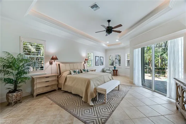 Bedroom with a tray ceiling, access to outside, ornamental molding, multiple windows, and light tile patterned floors