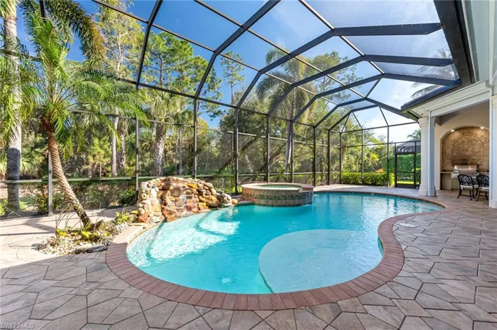 View of swimming pool featuring a pool with connected hot tub, a patio, and glass enclosure