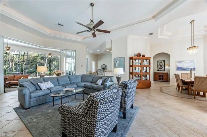 Living area featuring a tray ceiling, a ceiling fan, ornamental molding, light tile patterned flooring, and arched walkways