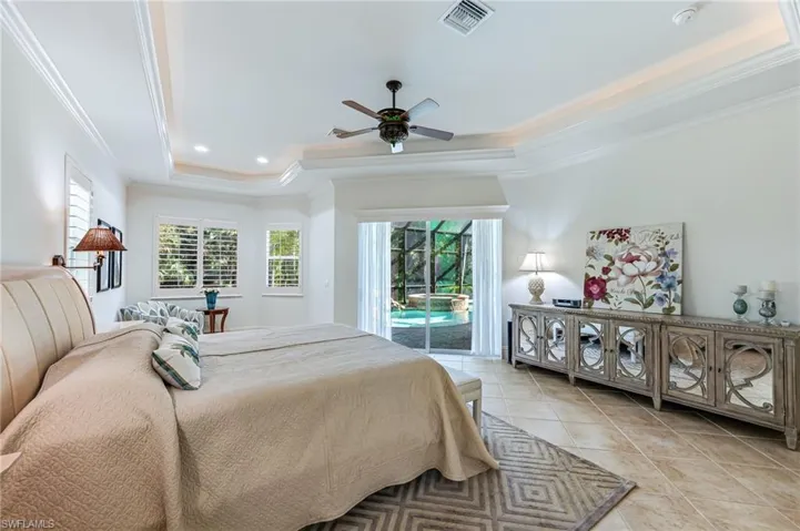 Bedroom featuring a tray ceiling, crown molding, access to exterior, multiple windows, and light tile patterned flooring