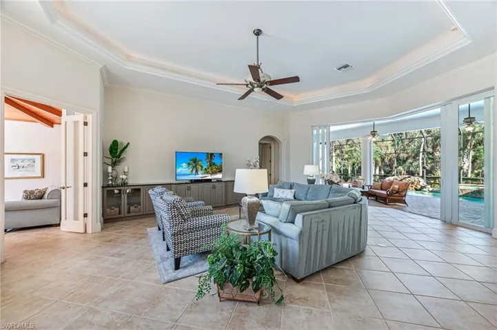 Living area with a tray ceiling, ceiling fan, crown molding, light tile patterned floors, and arched walkways