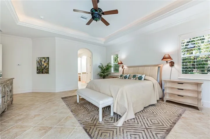 Bedroom with arched walkways, a tray ceiling, crown molding, light tile patterned flooring, and a ceiling fan