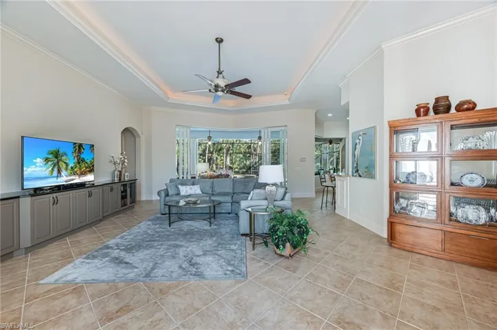 Living room with a ceiling fan, light tile patterned floors, arched walkways, a raised ceiling, and crown molding