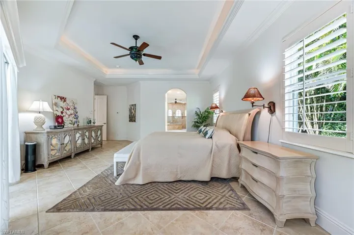 Tiled bedroom with a raised ceiling, crown molding, and ceiling fan