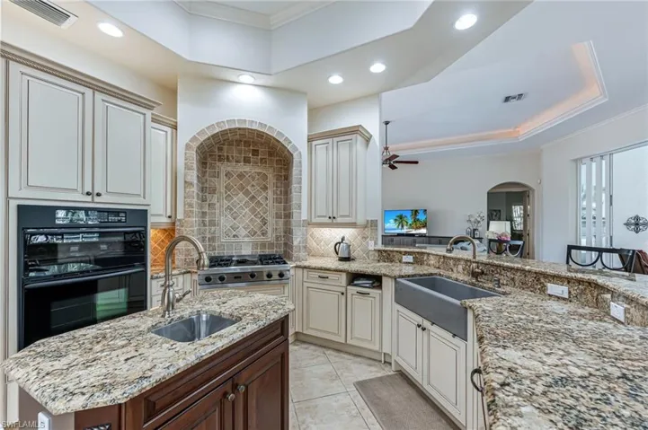 Kitchen with a tray ceiling, recessed lighting, arched walkways, decorative backsplash, and ornamental molding
